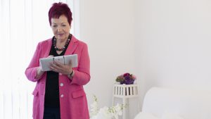 Karin Schwarz-Feuring bei der Arbeit mit dem Tablet. Rechtsanwältin Karin Schwarz-Feuring steht im Büro und arbeitet mit einem Tablet. Im Hintergrund sieht man Blumen.