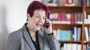 Rechtsanwältin Christel Karin Schwarz-Feuring am Telefon Frau Schwarz-Feuring telefoniert. Im Hintergrund steht ein Bücherregal.